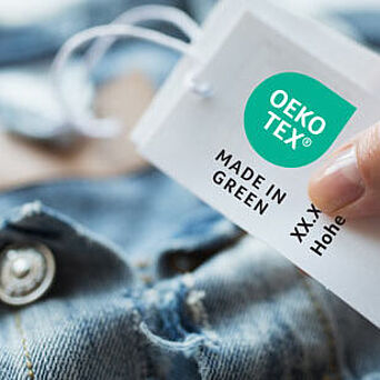 Denim jacket with hand holding an OEKO-TEX® MADE IN GREEN label tag