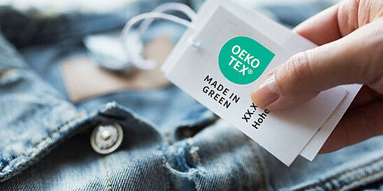 Denim jacket with hand holding an OEKO-TEX® MADE IN GREEN label tag