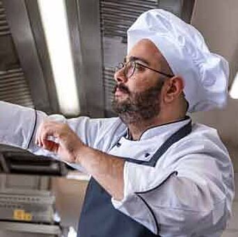 chef in kitchen wearing uniform, apron and hat