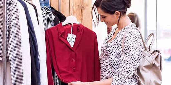 Shopper near rack of shirts, looking at a label