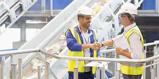 Auditor and textile worker wearing hardhats shaking hands