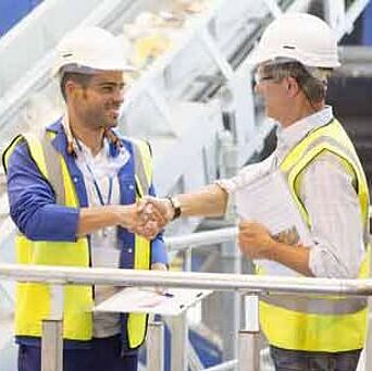 Auditor and textile worker wearing hardhats shaking hands