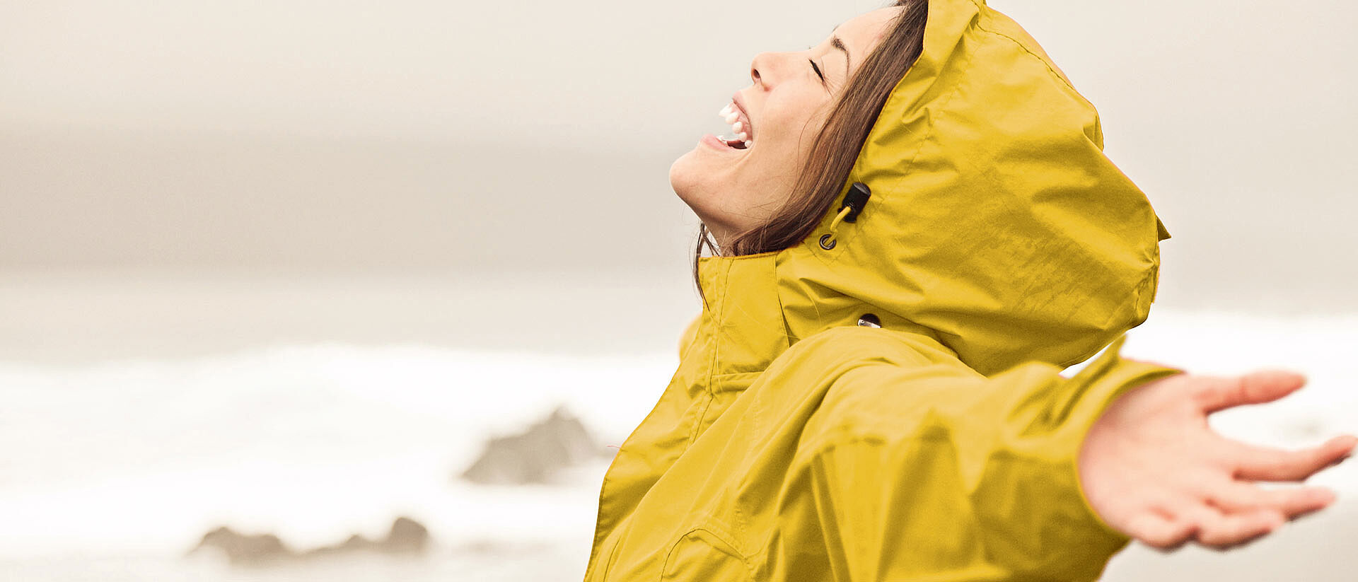 woman wearing yellow raincoat with arms spread