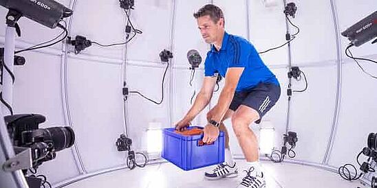 Man wearing athletic clothes and footwear, lifting crate in 4D scanner at Hohenstein