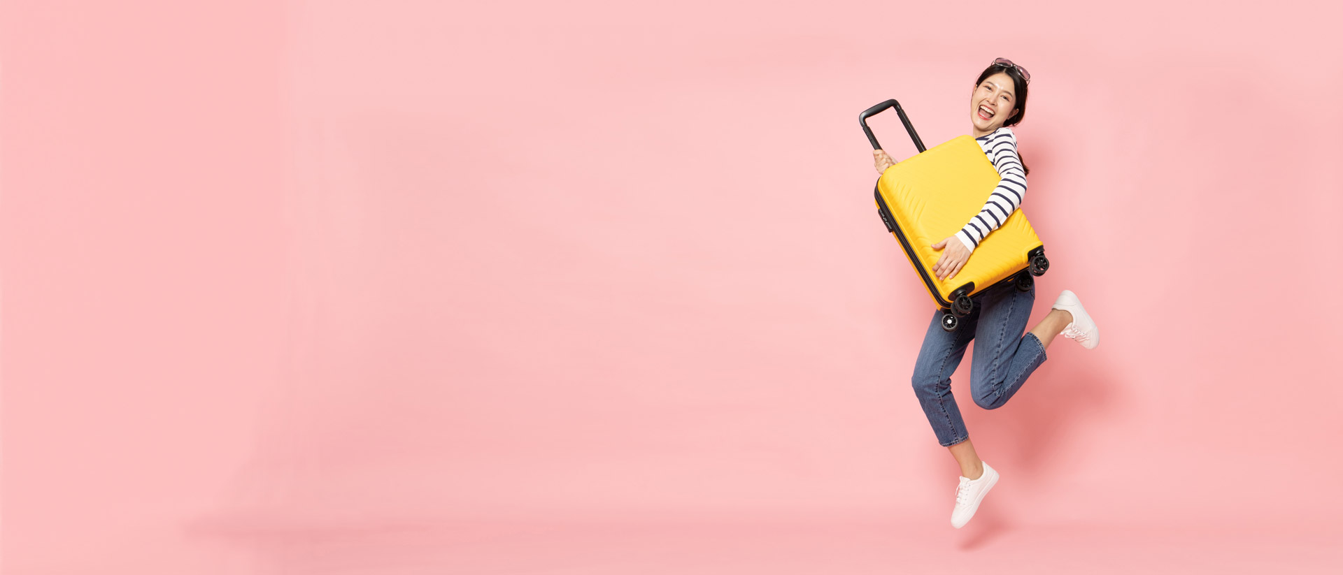 Woman holding a hard, yellow suitcase, wearing white shirt and shoes with jeans