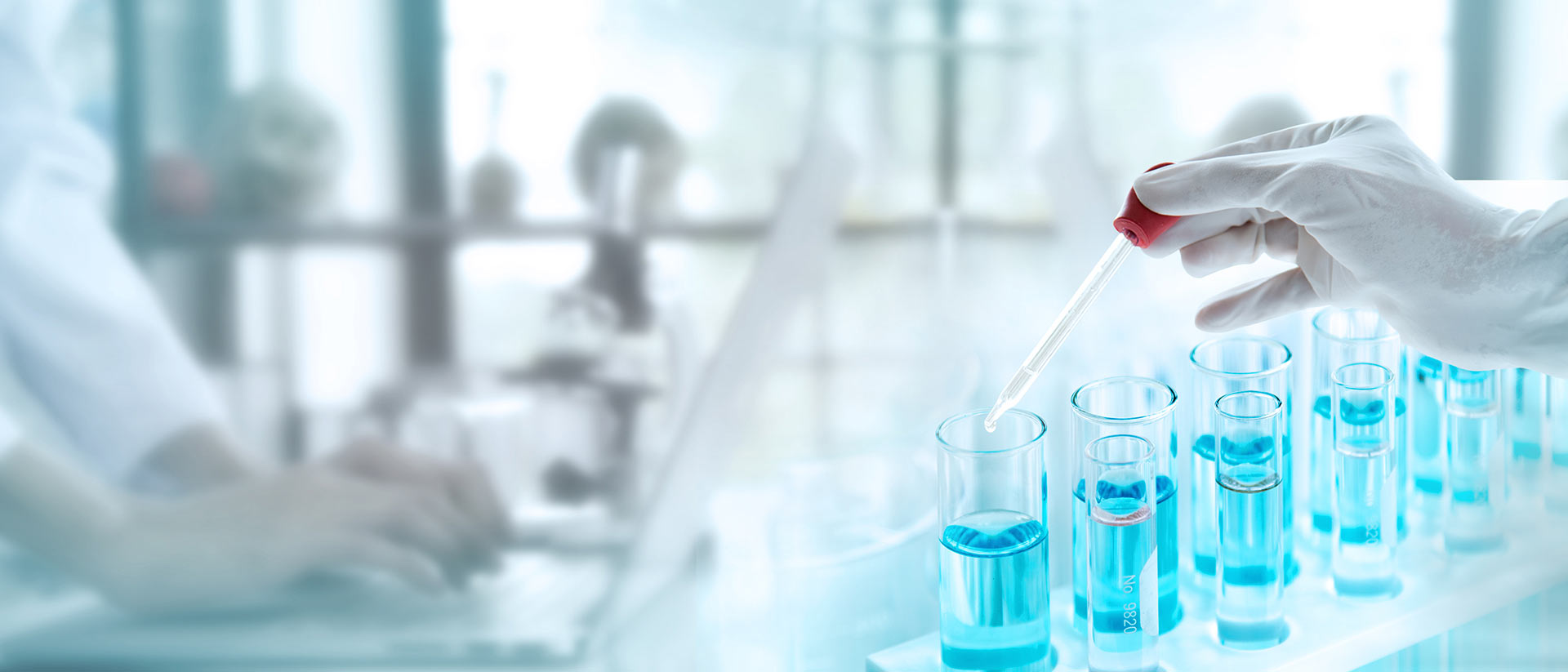 Chemical Characterization & E&L Testing for Medical Devices Gloved hand pipetting blue solvent into test tubes in a laboratory