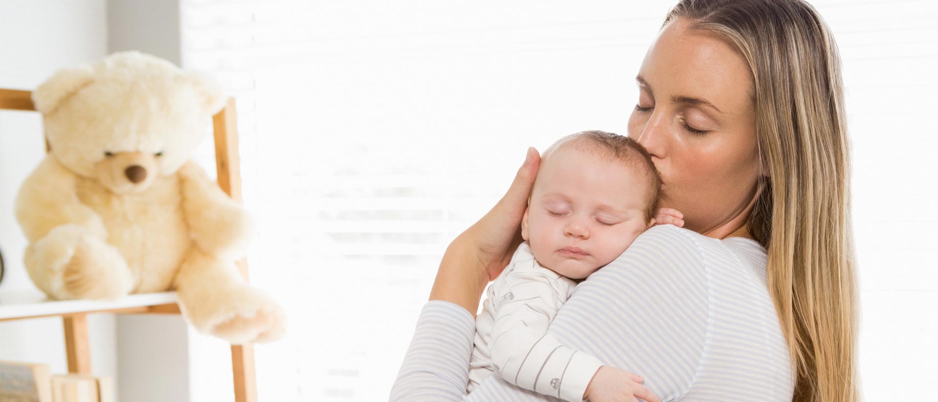 Mother holding baby near face in softly lit bedroom