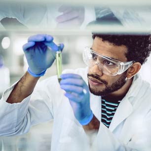 Man wearing blue gloves and lab coat holding vial of textile chemicals