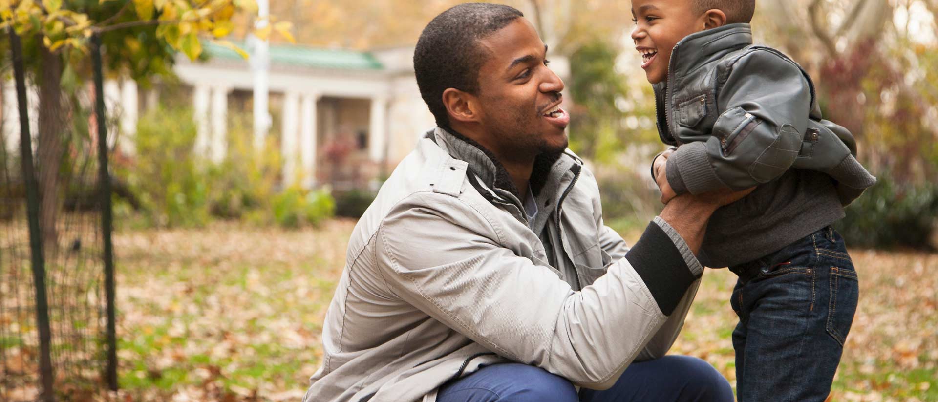 child and father wearing certified leather jackets in front of green trees