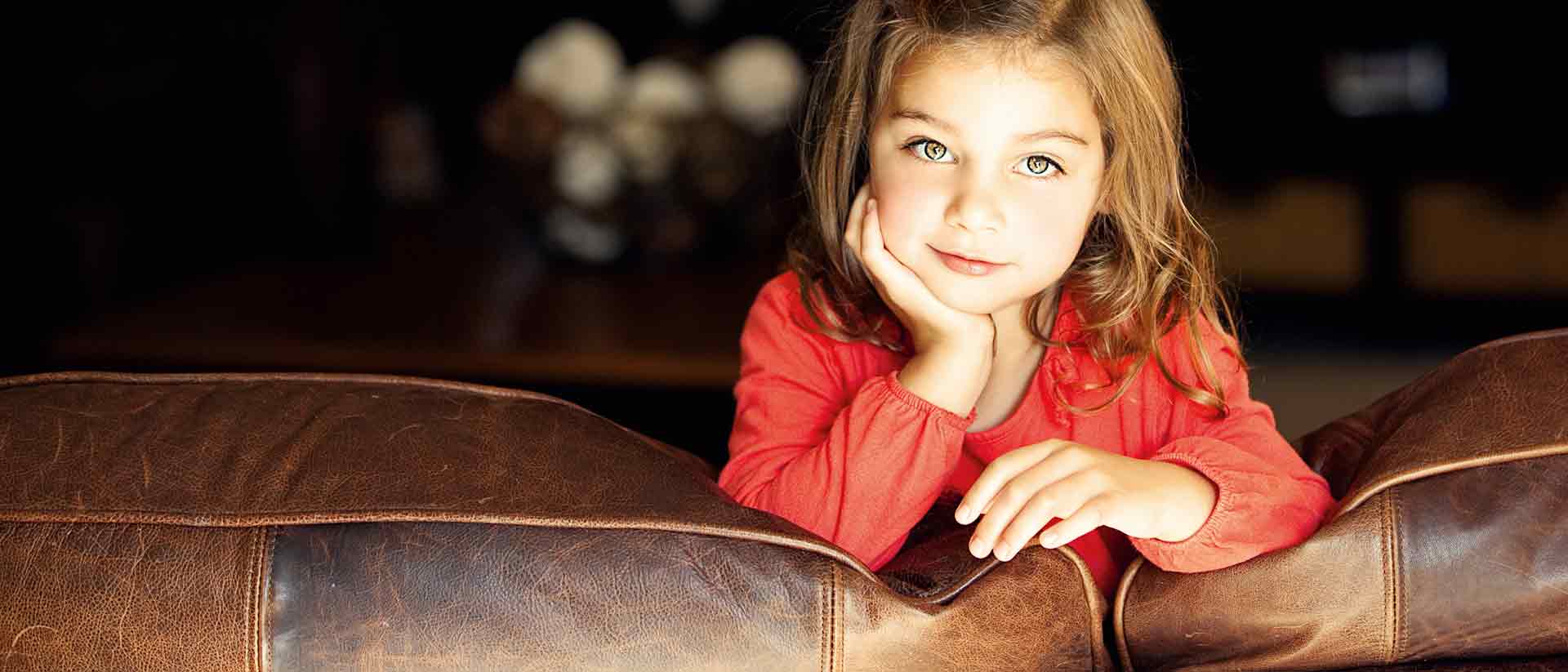 Girl in red shirt leaning on brown leather couch