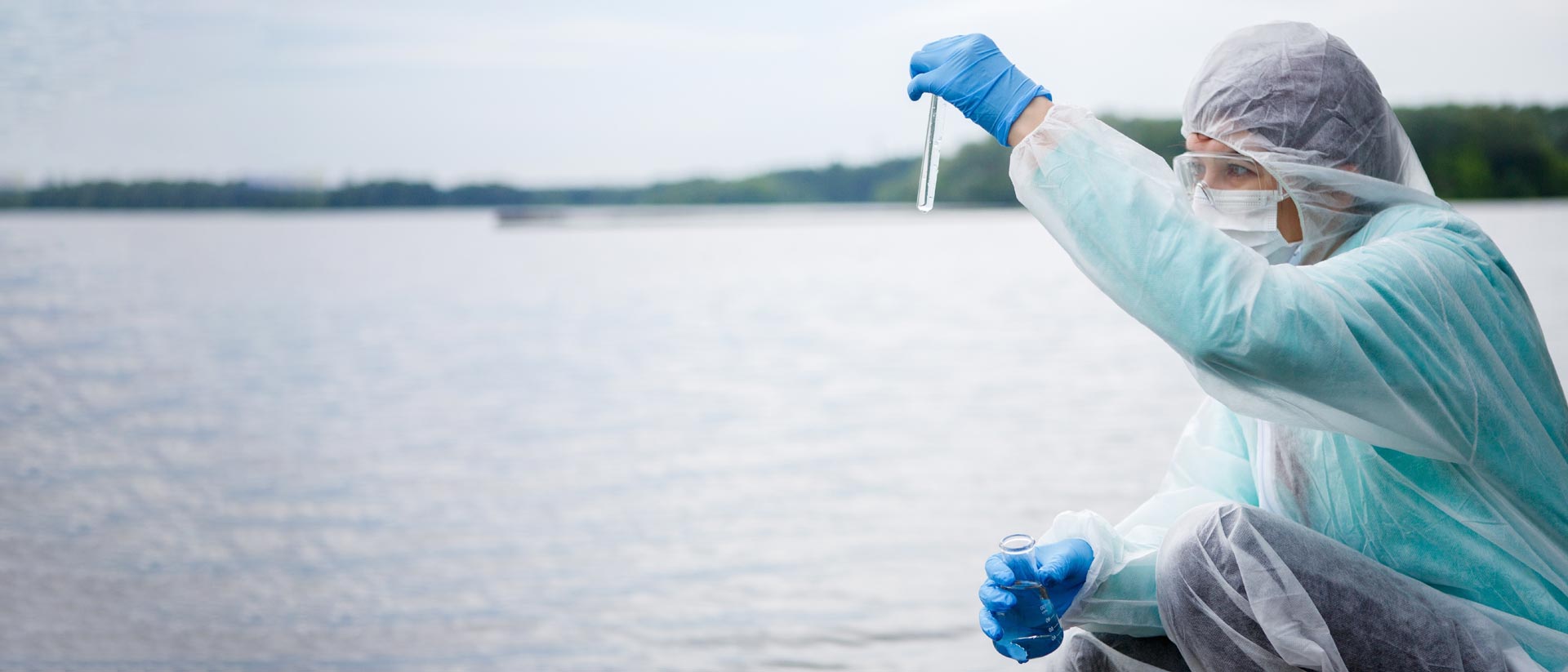 lab technician in protective gear, taking wastewater samples from a river.