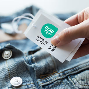 Hand holding a OEKO-TEX® MADE IN GREEN certification label attached to a denim jacket