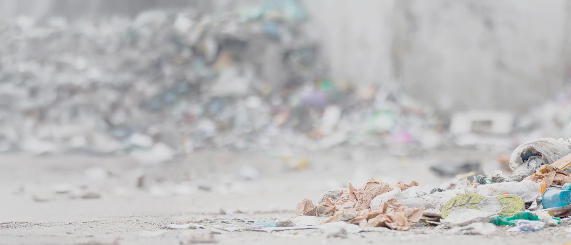 Discarded shoe, clothes and plastic bottles near a large pile of trash.