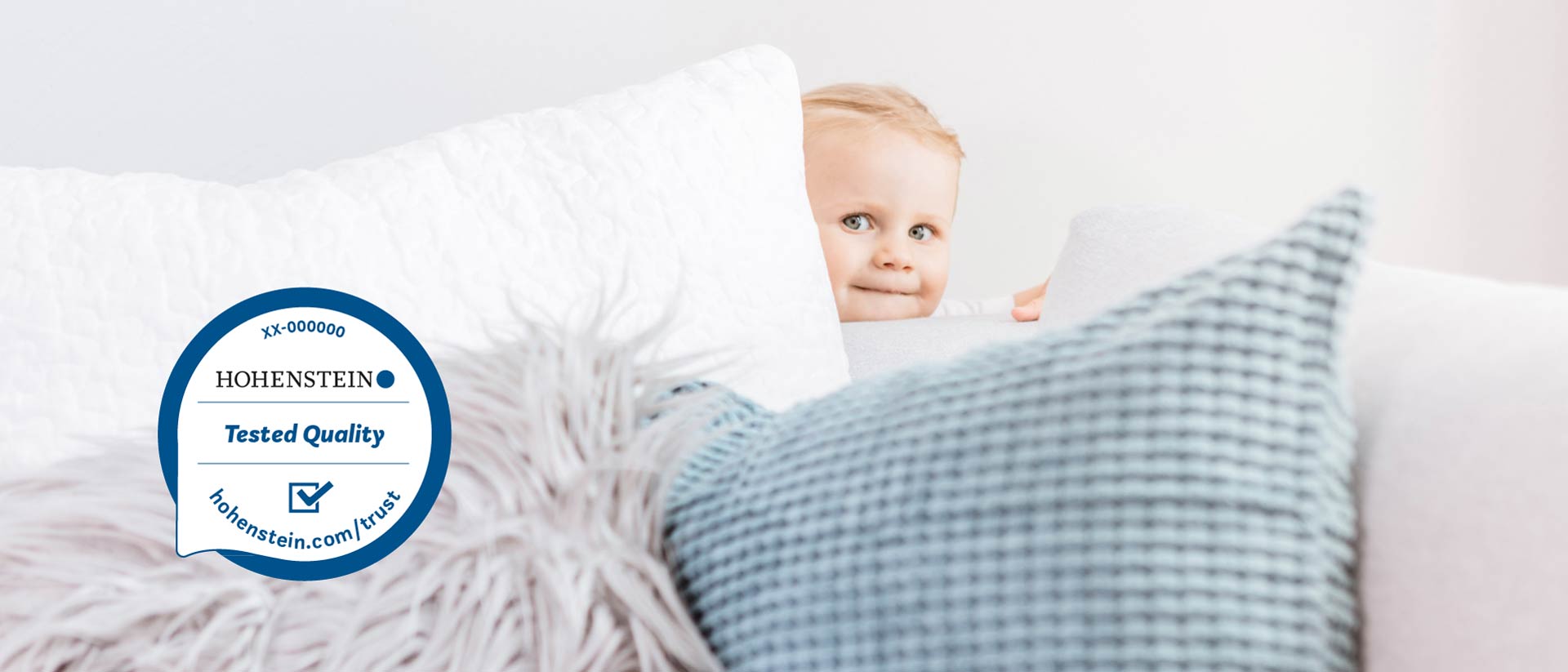 Child behind a couch with pillows and a Hohenstein Quality Label