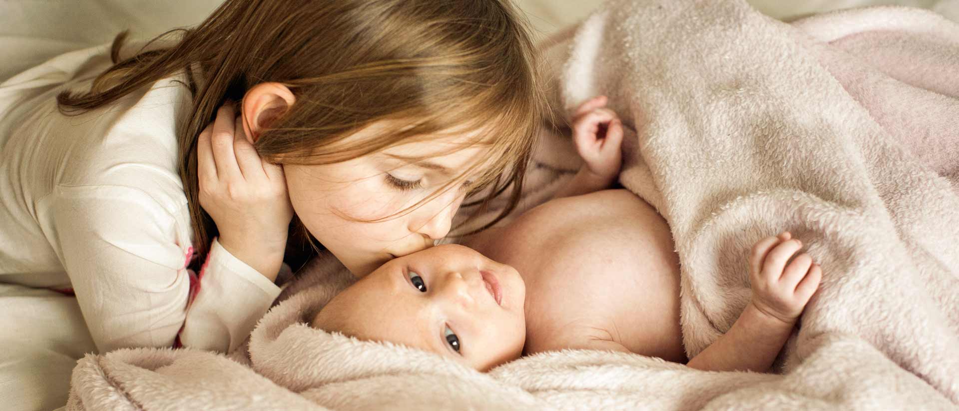 Girl in white shirt kissing baby who is wrapped in a blanket