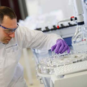 Lab worker with purple gloves and lab coat, examining vials of textile chemicals in the lab