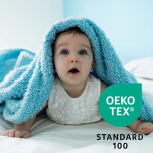 Baby on bed, wearing white shirt, covered by blue blanket