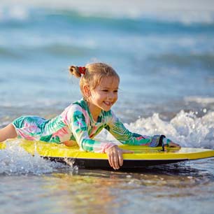 Girl in UV protective swimwear on surfboard at beach