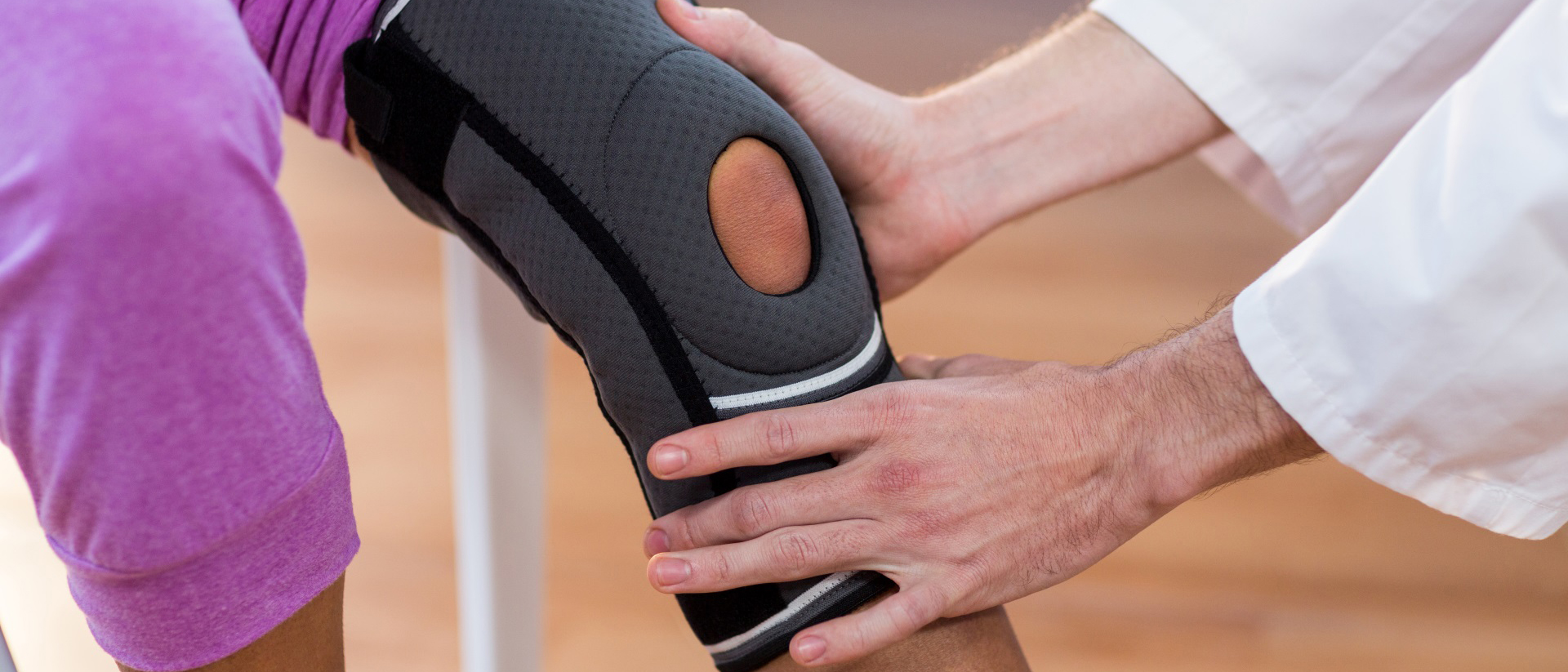 Patient wearing knee brace sitting with medical device expert holding knee