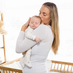 mom holding newborn near crib