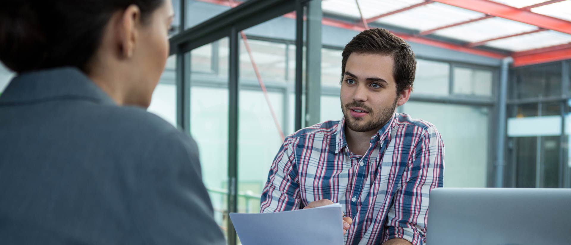 Two people talking at a table with a laptop and paper