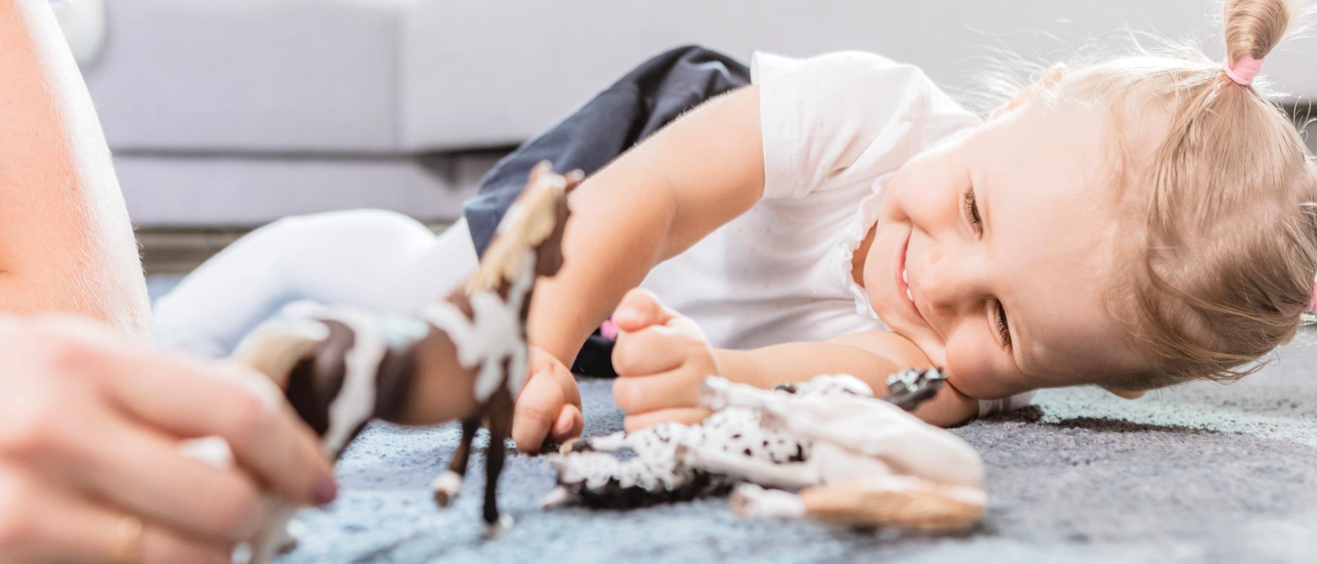 Girl playing with toy horses on blue carpet