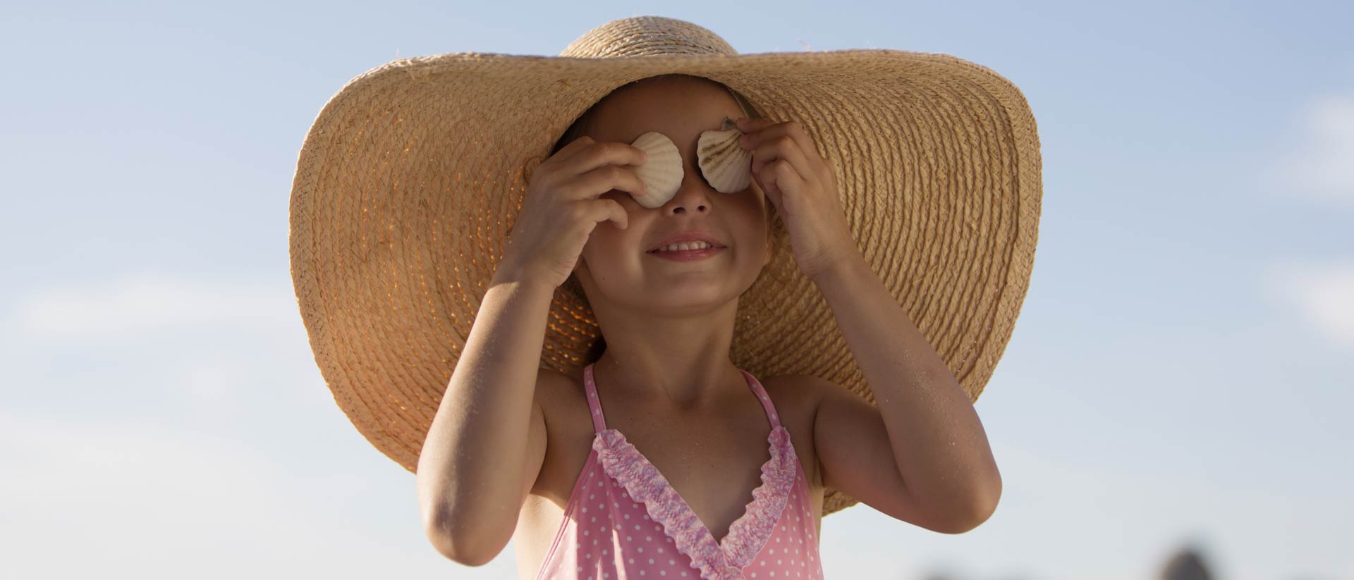 Girl in large sun hat and pink swimsuit on sunny day