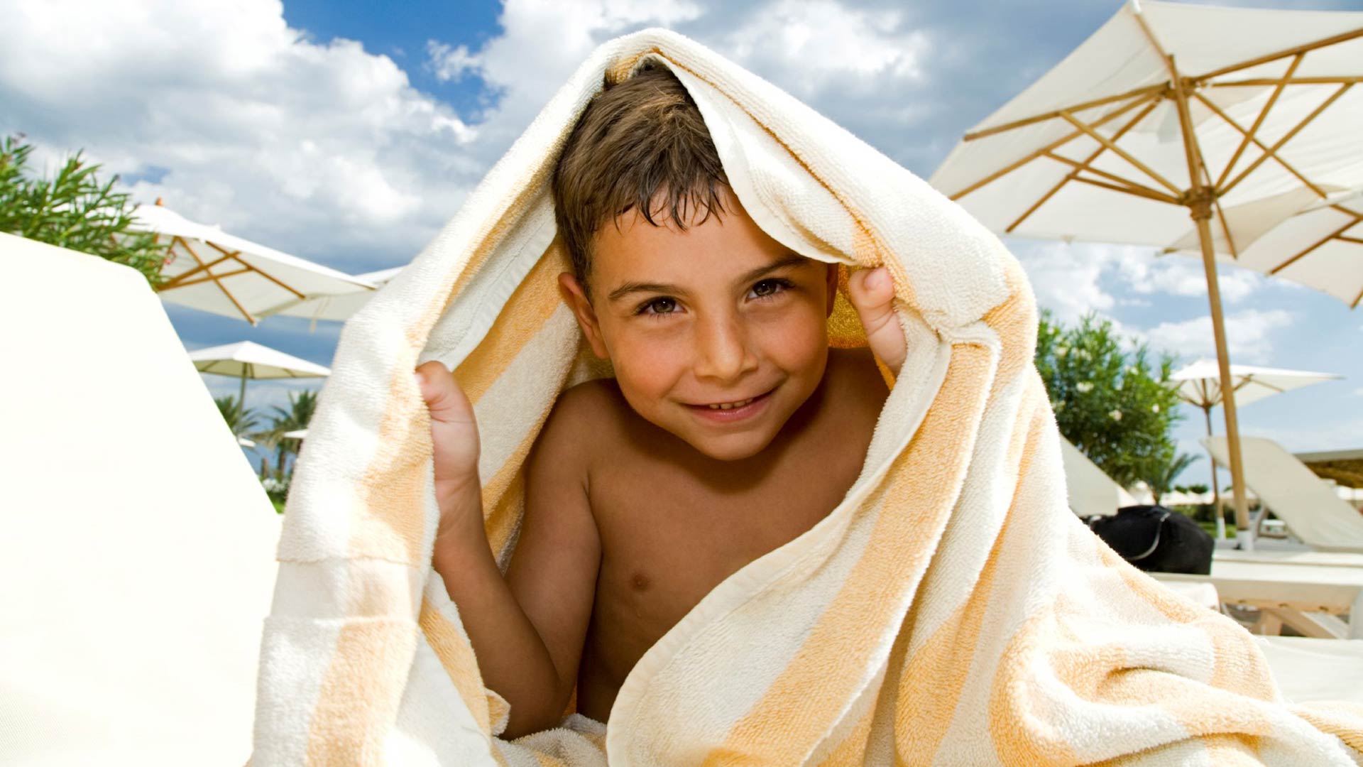 Child under striped towel on sunny day