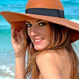 Woman on beach shielding sun with hat